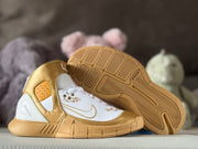 Gold and white shoes displayed with one outsole facing upward, showing the geometric tread pattern.