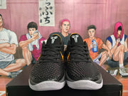 Front view of paired black basketball sneakers with textured uppers, black laces, white outsole sections and Kobe-associated tongue graphics.