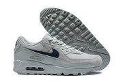 Grey and navy Nike Air Max 90 sneakers shown with a view of the patterned outsole.