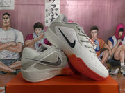 Angled view of gray Nike basketball sneakers with perforated panels, black Swoosh logos, and red soles.