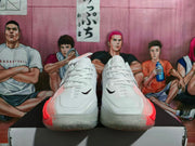 Front view of white Nike basketball shoes showing black Swoosh logos and pink-orange detailing.