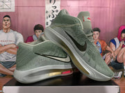 Angled view of green Nike GT-style basketball sneakers showing the black Swoosh, red tongue accents, and translucent soles.