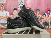 Angled view of two black sneakers highlighting the stitched side graphics, orange eyelets, and high-top collars.