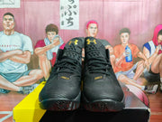 Front view of a pair of black basketball sneakers showing the lace-up construction, gold logos, and textured uppers.