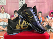 Angled view of the sneaker pair showing black uppers, purple forefoot panels, gold side graphics and Nike swoosh branding.