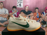 Side view of a cream Nike sneaker with a textured green Swoosh and translucent orange outsole.