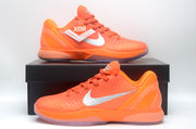 Bright orange Nike basketball sneaker displayed on a black shoe box, showing silver Swoosh branding and a translucent outsole.