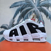 Close-up side view of a white and black Nike sneaker with a segmented white sole, visible cushioning elements, and red accents.