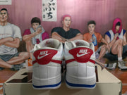 Rear view of white Nike low-top sneakers with red heel panels, blue outsole accents, and visible Nike branding.