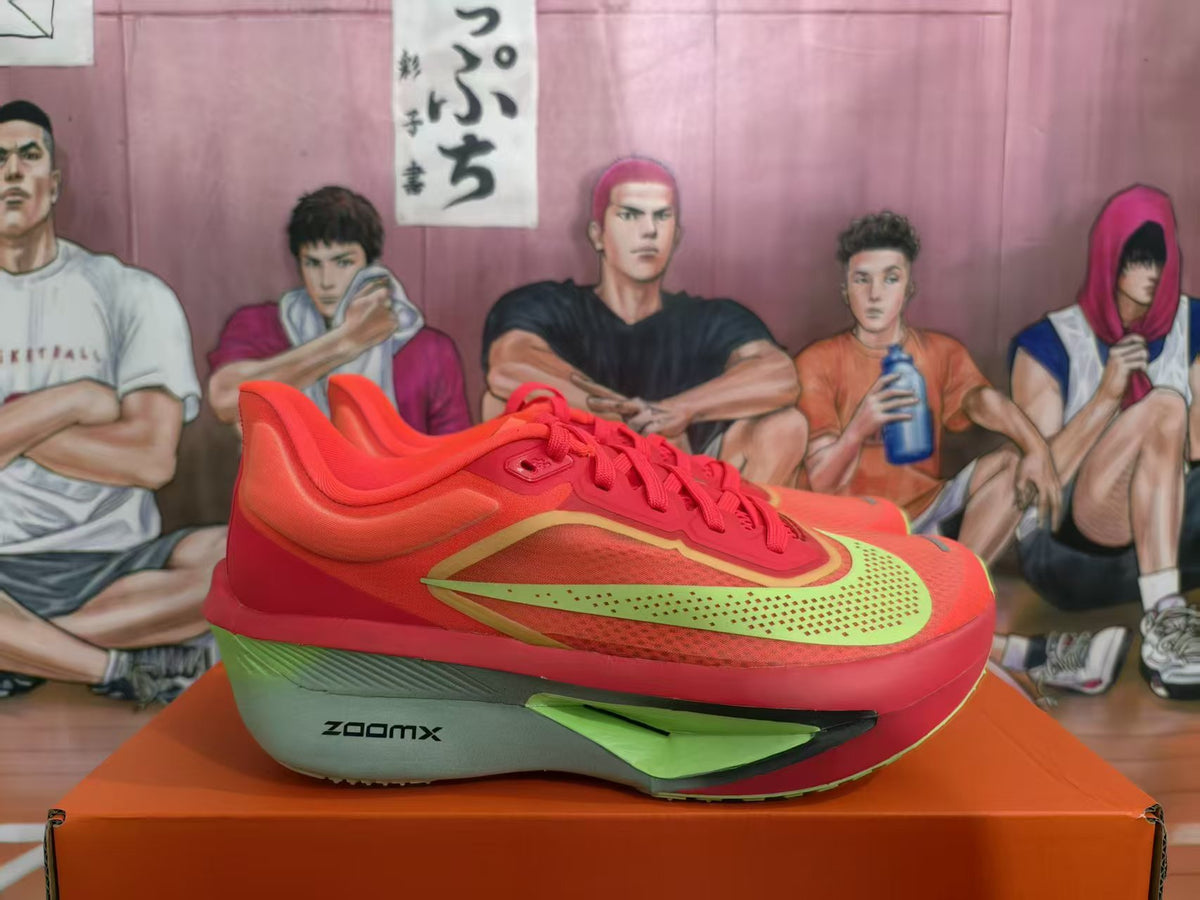 Side view of red Nike ZoomX sneakers with yellow and green accents displayed on an orange box.