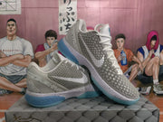 Angled view of a pair of white and grey basketball sneakers with textured side panels and blue outsoles.