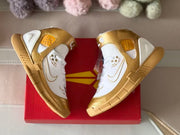 Top-down view of the paired shoes on a red shoebox, showing the white laces, gold overlays, and ankle straps.