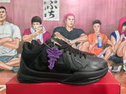 Side profile of a black basketball sneaker showing layered panels, textured detailing, and a purple hanging accessory.