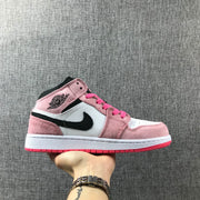 Side view of a pink, white and black Jordan Air Jordan 1 Mid sneaker held against a gray fabric background.