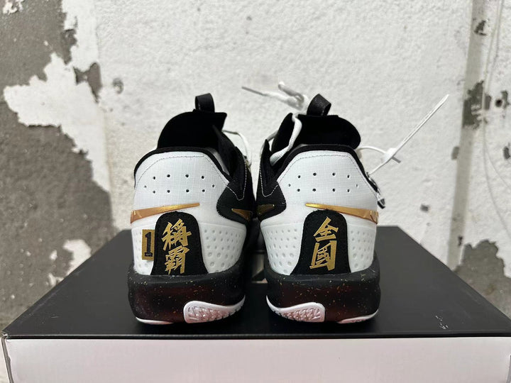 Rear view of white and black Nike basketball shoes with gold heel accents and black, speckled midsoles.