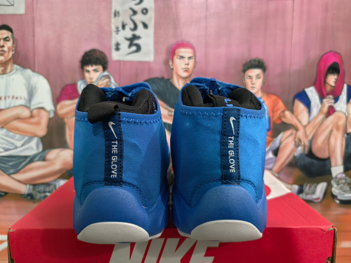 Rear view of blue Nike The Glove sneakers showing black collars, heel pull tabs, and white outsole sections on a Nike shoebox.