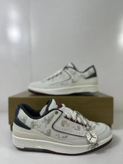 Angled close view of the white sneaker pair with dragon-pattern detailing and a hanging decorative charm.