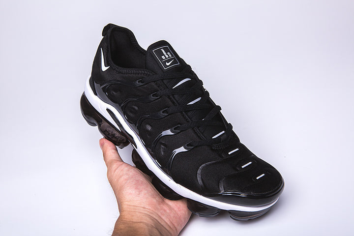 Black and white Nike TN-10 sneaker held at an angle, showing the side and sole.
