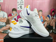 White Nike basketball sneakers arranged at an angle, showing purple branding, yellow heel accents, and textured soles.