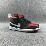 Low front-side view of the pair showing the mid-top shape, black laces, red toe panels, and red outsoles.