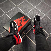 Top-down view of the pair beside a black Nike shoe box, showing black uppers with red accents.