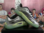Angled view showing the silver upper, black padded lining, patterned side panel, and green outsole area.