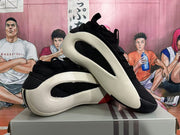 Two black, white, and red low-top sneakers arranged on top of a shoebox, showing their side profiles and outsole details.