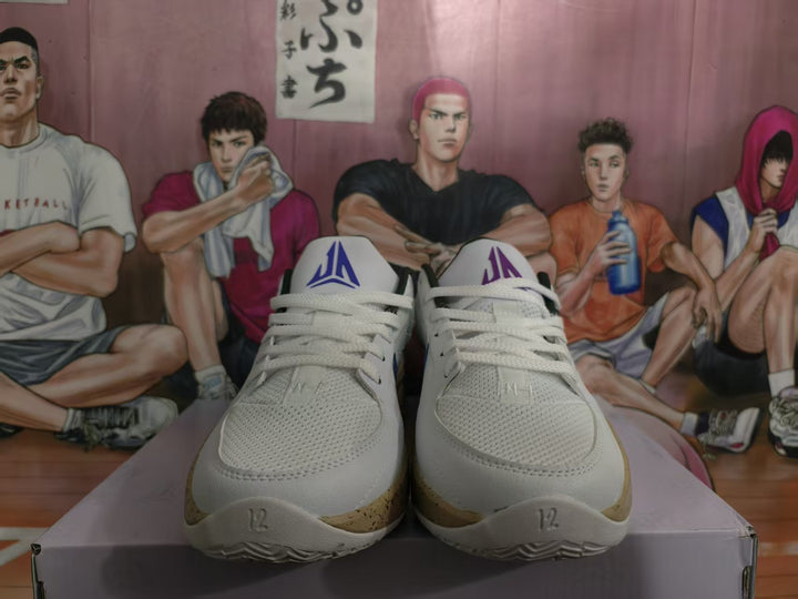Front view of white basketball sneakers with blue JA tongue branding and tan speckled soles.