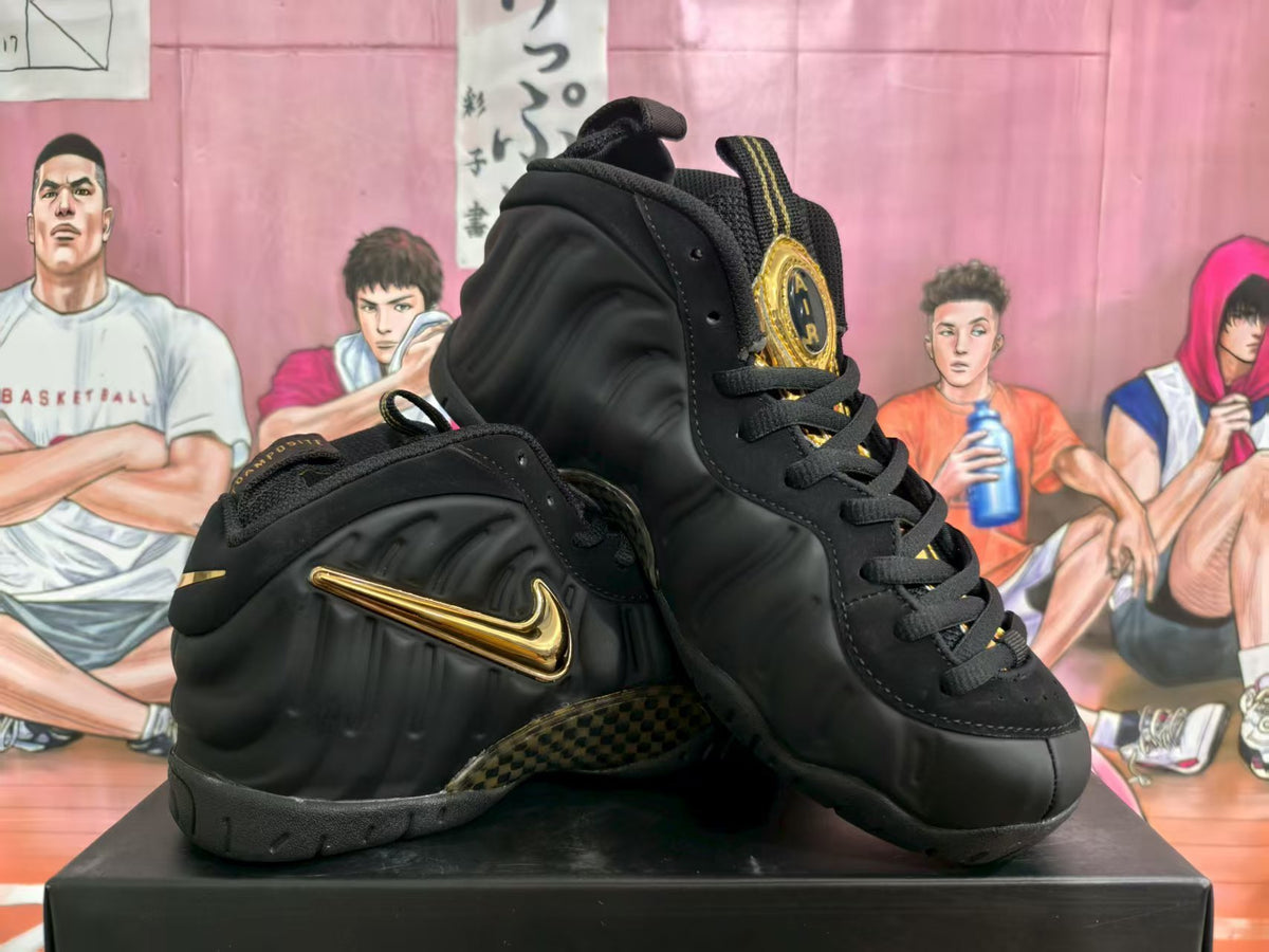 Black Nike Air Foamposite One high-top sneakers with gold-colored accents, shown at an angle.