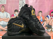Black Nike Air Foamposite One high-top sneakers with gold-colored accents, shown at an angle.