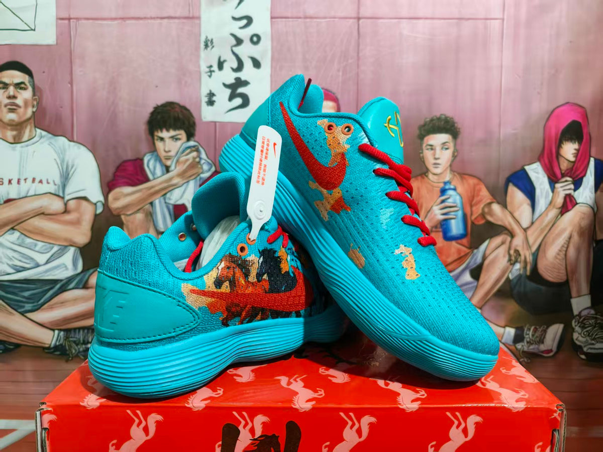 Pair of blue Nike basketball sneakers with red laces, multicolor graphic side panels, and a ribbed blue outsole displayed on a red box.