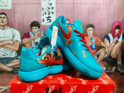 Pair of blue Nike basketball sneakers with red laces, multicolor graphic side panels, and a ribbed blue outsole displayed on a red box.