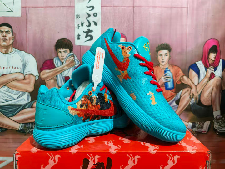 Pair of blue Nike basketball sneakers with red laces, multicolor graphic side panels, and a ribbed blue outsole displayed on a red box.