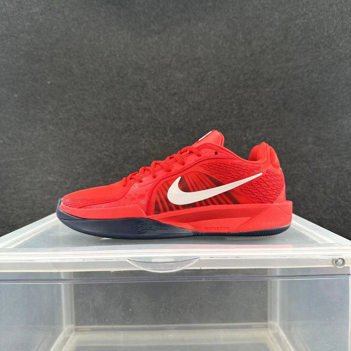Side view of a red Nike basketball-style sneaker with a white Swoosh and dark outsole displayed on a clear stand.