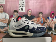 Side view of a white and navy Nike basketball sneaker with green heel detailing, white laces, perforations, and visible ZoomX midsole text.