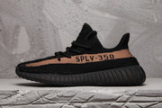 Side profile of a black Yeezy 350 V2-style sneaker with a peach-toned stripe, SPLY-350 lettering, and ribbed outsole.