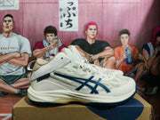 Side view of cream ASICS basketball sneakers with navy logos and high-cut ankle collars.