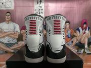 Rear view of the white and black high-top basketball sneakers showing red tongue detailing and heel graphics.
