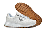 White Prada sneakers shown from the side and underside, highlighting the lugged gum-colored tread.