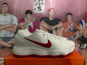 Side profile of a white Nike sneaker showing the red Swoosh, gold-tone eyelets and textured red outsole.