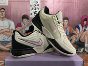 Angled view of the beige and black basketball sneaker pair with pink detailing