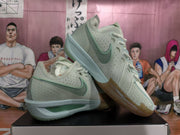 Angled view of a pair of green Nike basketball sneakers showing the side Swoosh, perforated panels, cream laces, and gum-colored outsole.