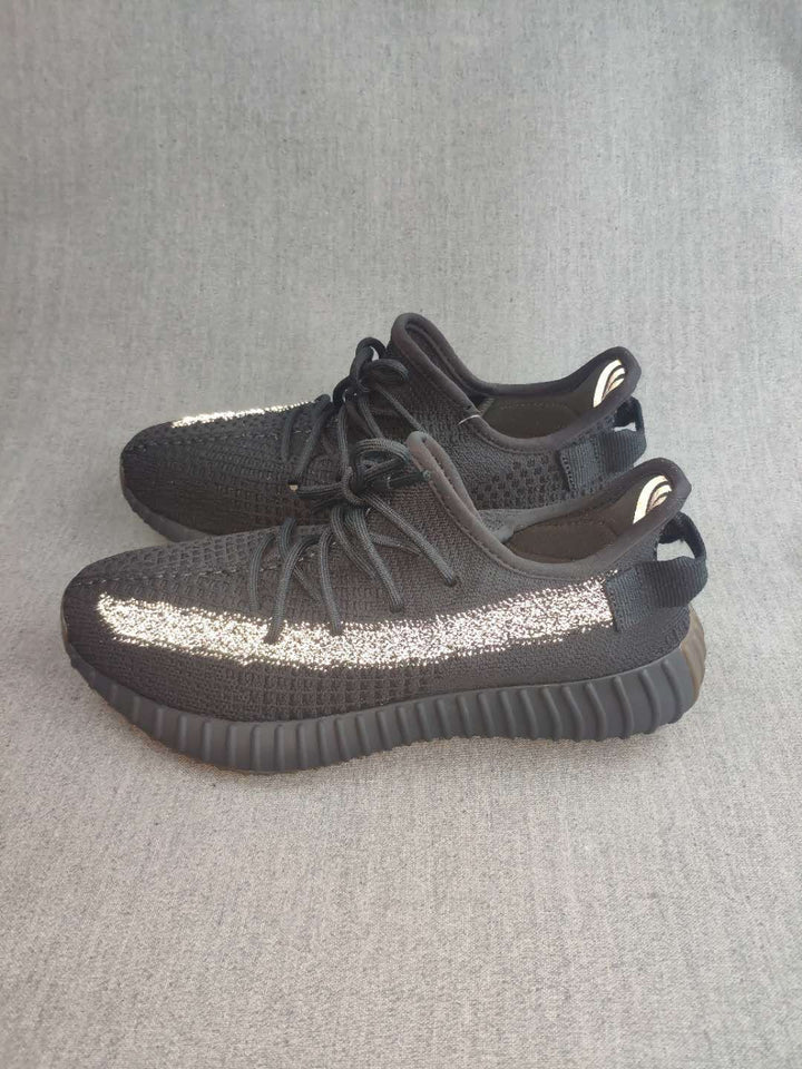 Pair of black Yeezy 350 V2-style sneakers shown from the side, featuring reflective side stripes and ribbed outsoles.