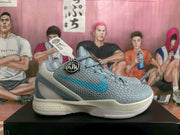 Side view of grey and blue Nike Caitlin PE basketball sneakers showing the textured upper, blue Swoosh and layered sole.