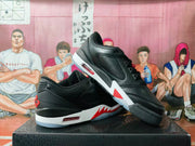 Angled view of black low-top sneakers showing perforated panels, white midsoles, red accents, and visible heel cushioning windows.