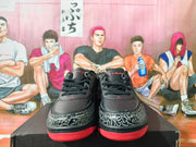 Front view of black lace-up sneakers with patterned toe overlays and red outsole.