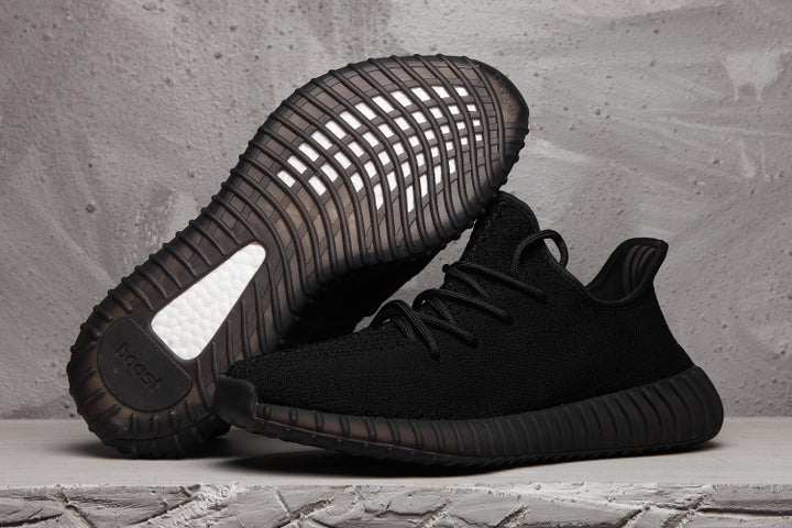 Pair of black Yeezy 350 V2 style sneakers, with one shoe showing the ribbed outsole.