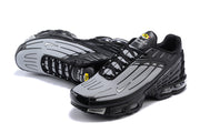 Angled view of black and grey Nike Air Max Plus sneakers.