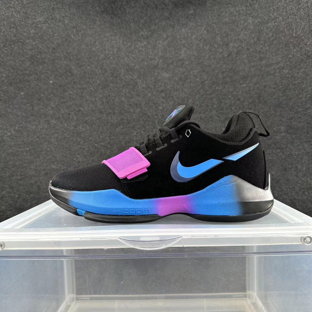 Side view of a black Nike sneaker with a blue Swoosh, pink forefoot strap, and blue and pink sole accents.