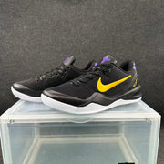 Pair of black Nike basketball sneakers with gold Swooshes, purple accents, and white outsoles shown from a three-quarter angle.